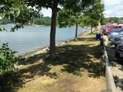 A tree-lined grassy space between a river and a parking area